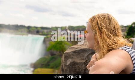 Bionda Tourist ragazza che guarda alle Cascate del Niagara il grande canadese Punto di riferimento americano in Ontario, la famosa cascata negli Stati Uniti Bordo con ferro di cavallo Foto Stock