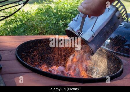 Camino BBQ fuoco di carbone avviatore pieno di bricchetti che bruciano essere gettato in una griglia all'aperto con scintille che volano Foto Stock