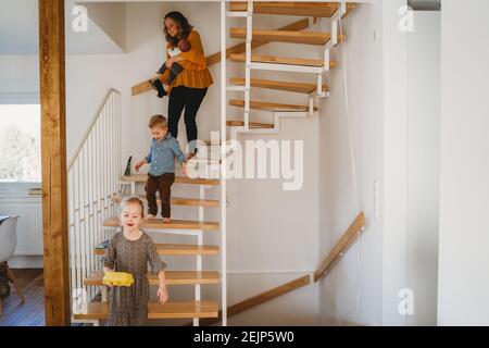 Mamma e bambini che camminano giù per le scale a casa durante quarantena Foto Stock