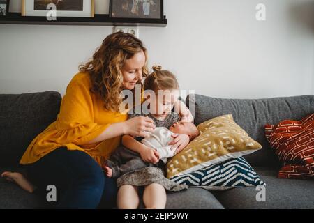 Mamma e figlia seduti sul divano che tiene il bambino in vita camera a casa Foto Stock