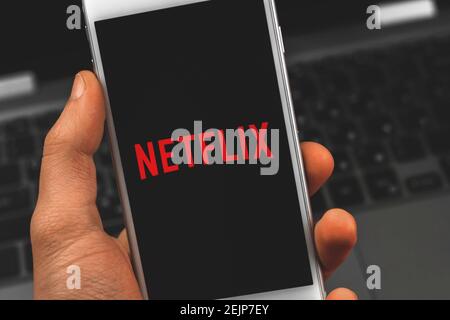 Kharkov, Ucraina - 22 febbraio 2021: Uomo che detiene smartphone Apple con applicazione Netflix, logotipo di servizio di streaming primo piano foto Foto Stock