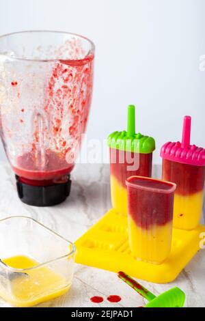 Primo piano immagine isolata di muffe ghiacciate su un vassoio pieno di purea di frutti di bosco e mango fatti in casa con il recipiente di vetro sullo sfondo. La miscela in Th Foto Stock