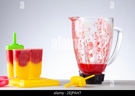 Primo piano immagine isolata di muffe ghiacciate su un vassoio pieno di purea di frutti di bosco e mango fatti in casa con il recipiente di vetro sullo sfondo. La miscela in Th Foto Stock