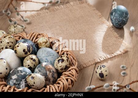 Composizione di Pasqua - uova di Pasqua dipinte con coloranti naturali in un nido di vimini su un tavolo di legno, copyspace. Foto Stock