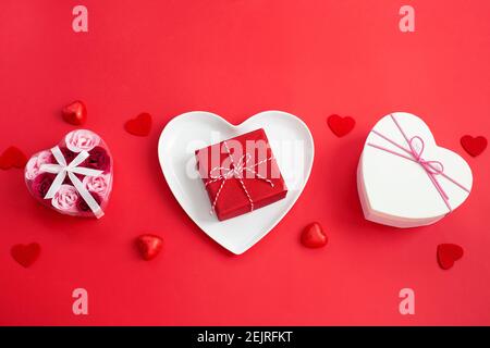 Piastra bianca a forma di cuore e diverse scatole regalo. Impostazione del tavolo per le feste. Regalo di San Valentino Foto Stock