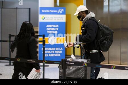 Mississauga, Canada. 22 Feb 2021. Un viaggiatore che indossa una maschera facciale cammina con i suoi bagagli verso un sito di test COVID-19 dopo essere arrivato all'aeroporto internazionale di Toronto a Mississauga, Ontario, Canada, il 22 febbraio 2021. A partire da Lunedi', i viaggiatori che arrivano in Canada in aereo sono tenuti a fare un test molecolare COVID-19 prima di uscire dall'aeroporto. Gli ospiti sono inoltre tenuti a mettere in quarantena per tre giorni in un hotel designato dal governo a proprie spese fino a quando non ottengono un risultato. Credit: Zou Zheng/Xinhua/Alamy Live News Foto Stock