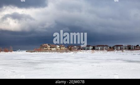 Un vecchio ponte di legno attraversa una sezione del lungomare congelato Georgian Bay a Collingwood, Ontario. Il cielo sopra è minaccioso e cupo, con un inverno Foto Stock