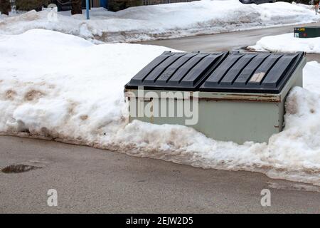 Un grande bidone di rifiuti di metallo si trova sul lato di una strada in una società condominio per i residenti di smaltire la loro spazzatura. Il bidone è vecchio e arrugginito, e. Foto Stock