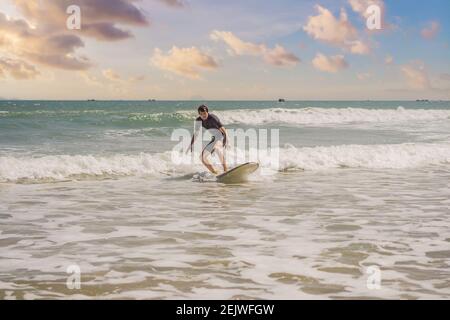 Giovani surfisti imparano a navigare in muta nera, giornata di sole sulla spiaggia dell'oceano Foto Stock