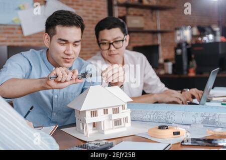 Le mani di ingegneria tengono il calibro a corsoio che lavora e che controlla la scala del modello della casa tra l'incontro con l'uomo d'affari e la donna d'affari. Architettura, motore Foto Stock