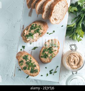 Vista superiore della fetta di pane con fatti in casa Turchia pate e fresco prezzemolo verde su bianco rustico scheda kutting su cemento bianco sfondo, Shallow DOF. Messa a fuoco selettiva Foto Stock