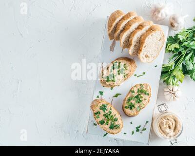 Vista superiore della fetta di pane con fatti in casa Turchia pate e fresco prezzemolo verde su bianco rustico scheda kutting su cemento bianco sfondo, Shallow DOF. Messa a fuoco selettiva copia spazio. Foto Stock