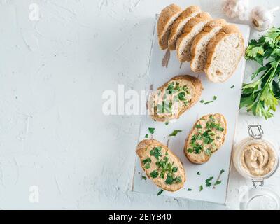 Vista superiore della fetta di pane con fatti in casa Turchia pate e fresco prezzemolo verde su bianco rustico scheda kutting su cemento bianco sfondo, Shallow DOF. Messa a fuoco selettiva copia spazio. Foto Stock
