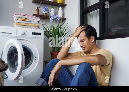 Casalinghi. Ha sottolineato l'uomo asiatico facendo lavanderia a casa caricando i vestiti in lavatrice Foto Stock