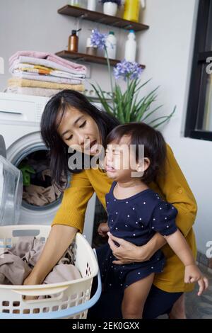 madre una casalinga con un bambino piangente in lavanderia a casa Foto Stock