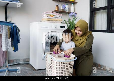 bella donna musulmana asiatica facendo lavanderia con suo figlio insieme Foto Stock