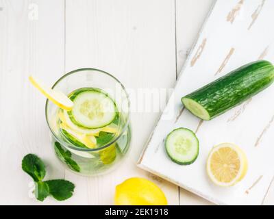 Acqua detox infusa con cetriolo, limone e menta in bottiglia di vetro su tavola bianca. Dieta, alimentazione sana, concetto di perdita di peso. Spazio di copia. Vista dall'alto o piatta. Foto Stock