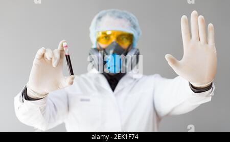 Il ricercatore tiene una provetta con sangue contaminato e mostra un gesto di arresto con l'altra mano. Concetto di ricerca per la prevenzione dei virus Foto Stock