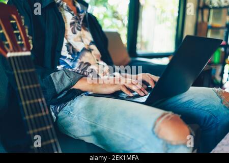 Uomo a mano usa il portatile per cercare la prenotazione di una vacanza sul divano a casa. Foto Stock