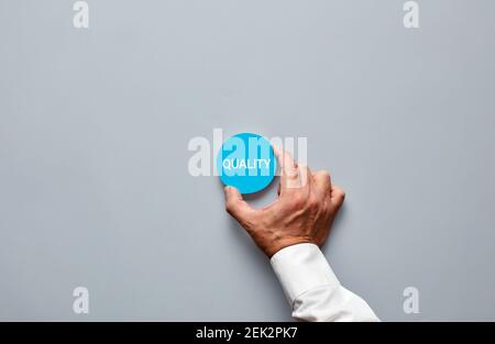 Mano di uomo d'affari che tiene un distintivo blu con la qualità di parola scritta su esso. Qualità del marchio, del servizio o del prodotto nel concetto aziendale. Foto Stock