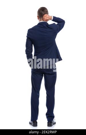 confuso elegante ragazzo in blu navy tuta tenendo la mano in tasca, graffiando testa e pensare, in piedi isolato su sfondo bianco in studio Foto Stock