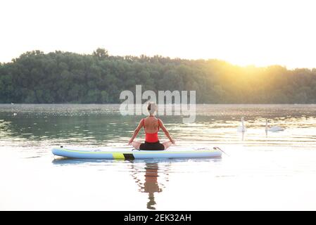 Donna che medita e pratica yoga durante l'alba su una tavola da paddleboard Foto Stock