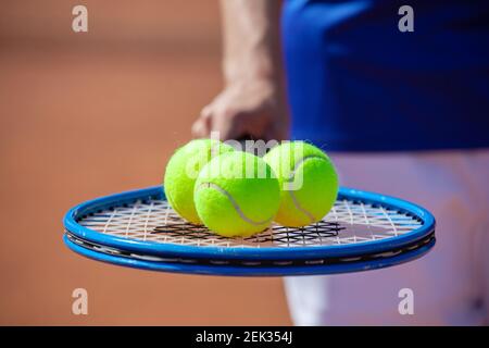 Giocatore di tennis che tiene una racchetta da tennis con tre palle sopra esso Foto Stock