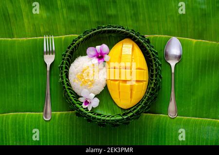 Dessert tailandese - riso al mango appiccicoso su piatto di foglie di banana con forchetta e cucchiaio messo su sfondo di foglia di banana. Foto Stock