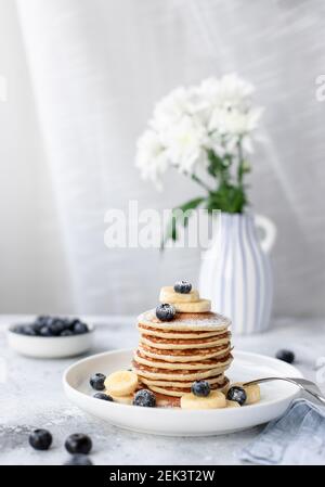 frittelle con mirtilli e banana sul tavolo con fiori Foto Stock