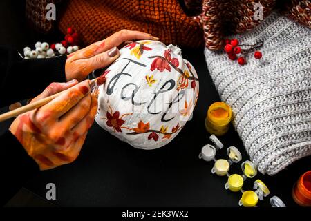 FAI DA TE. Fai da te. Donna dipinge decorazioni di ringraziamento su zucca arancione per Halloween. Vendemmia autunnale. Maglione casa accogliente. Pennello Foto Stock