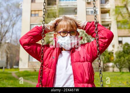 Bambina in maschera medica e guanti è oscillare da sola gesturing preoccupazione circa il virus COVID-19, Corona. Foto Stock