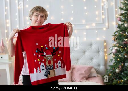 Una donna anziana prova su un maglione rosso di festa a Natale. Foto Stock