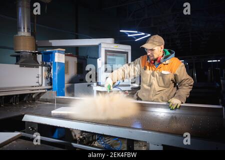 Un lavoratore di produzione di mobili in una macchina di taglio fa parti di mobili. Produzione di mobili. Foto Stock