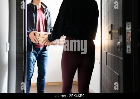 Consegna pizza a porta. Ristorante consegna cibo a casa. Corriere che dà scatole alla giovane donna felice. Deliverer a casa del cliente. Pranzo facile e veloce. Foto Stock