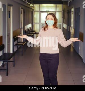 Donna adulta si alza con le braccia spalancate ai lati nella lobby di un ospedale senza pazienti. Il problema di ammettere le persone alla clinica du Foto Stock