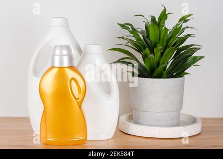 Bottiglie di detersivo e ammorbidente per tessuti con pianta verde in pentola di cemento sul tavolo. Contenitori di prodotti per la pulizia. Detergente liquido e conditi Foto Stock