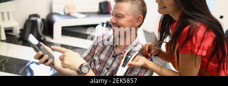 Cliente mostra al parrucchiere acconciatura al telefono e sorriso. Foto Stock