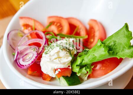 Insalata di verdure con pomodoro, cetriolo, peperone, cipolla e panna acida sul piatto bianco. Primo piano, messa a fuoco selettiva Foto Stock