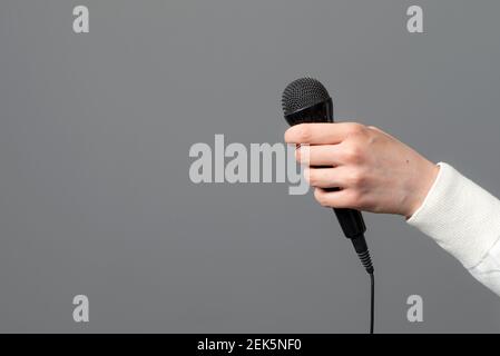 mano femminile con microfono su sfondo grigio, primo piano Foto Stock