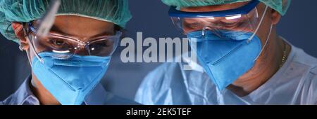 Uomo e donna in abiti da lavoro e maschera stare fianco a fianco e guardare. Foto Stock