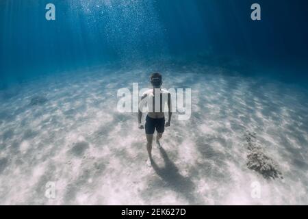 Uomo sportivo freediver rimanere sul fondo di sabbia sott'acqua in mare tropicale. Foto Stock