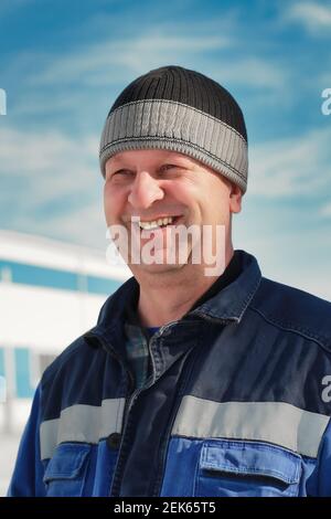 Un uomo in tute e un cappello si trova sulla strada contro il cielo. Ritratto di un vero lavoratore. Derisione Foto Stock