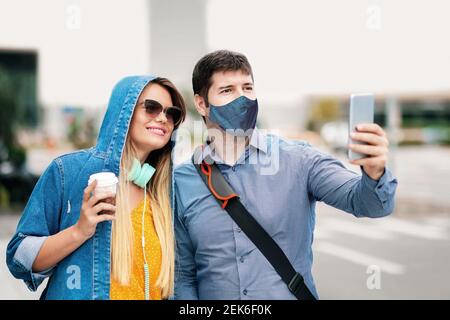 Felice fidanzato e ragazza che si divertono a prendere selfie con il viso maschera sulla strada della città Foto Stock