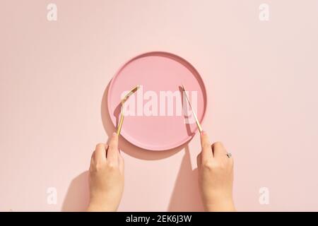 Le mani tengono una forca e un coltello sulla piastra di colore rosa sfondo Foto Stock