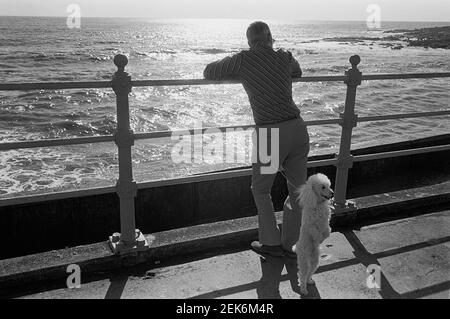 Un uomo e il suo cane sull'Esplanade a Porthcawl, Galles del Sud, 1977 Foto Stock