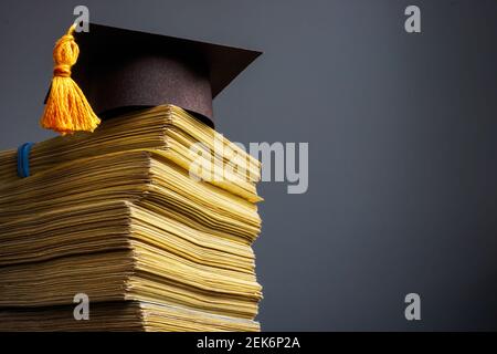 Concetto di costo dell'istruzione. Cappellino di laurea e stack di denaro per l'università. Foto Stock