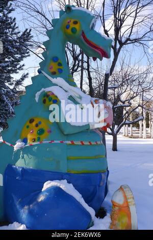 Giocattolo da dinosauro al parco giochi per bambini sotto la neve Foto Stock