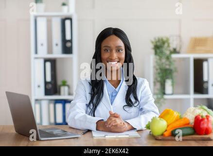 Alimentazione intelligente e alimentazione sana. Ritratto di un dietologo nero positivo che guarda la fotocamera e sorride sul posto di lavoro Foto Stock