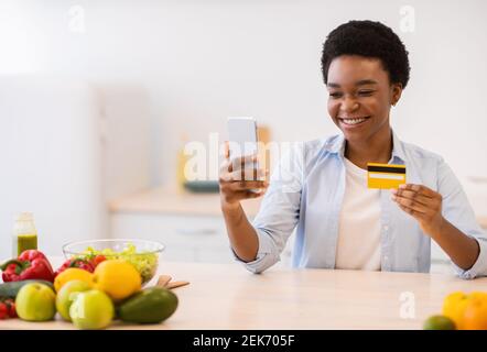 Donna che usa la carta di credito e il telefono acquistare alimentari in cucina Foto Stock