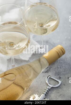 Due bicchieri di cristallo e una bottiglia di vino bianco fatto in casa con cavatappi in acciaio su sfondo chiaro. Foto Stock